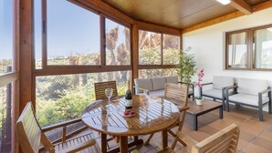 En overdækket terrasse med et træbord og stole, en sofa og en potteplante.