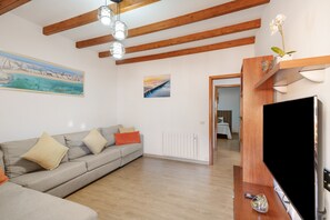 Un salon avec un canapé, une télévision, des poutres en bois et des œuvres d’art accrochées aux murs.
