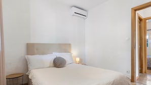 A bedroom with a bed, bedside table, lamp, and an air conditioning unit.