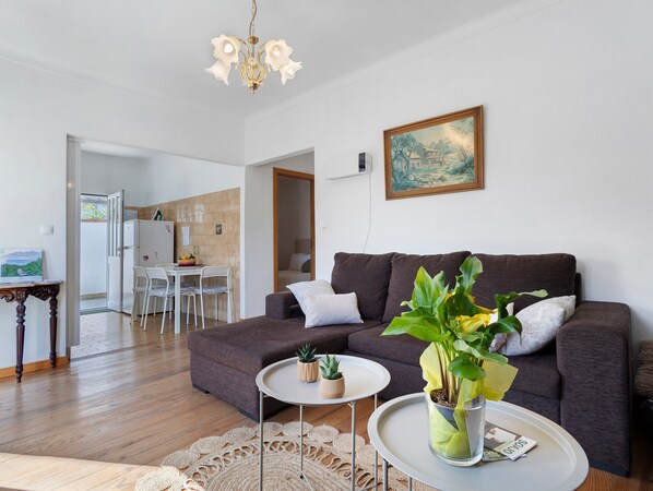 Un salon comprenant un canapé, une table basse, un coin repas avec des chaises, et une cuisine à l’arrière-plan.