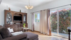 A living room with a sofa, television, wooden cabinet, and a large window with curtains.