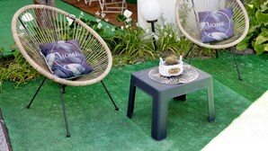 Two wicker chairs with cushions, a small table with a potted plant, and a green artificial turf area.