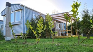 Ein Wohnhaus mit überdachter Veranda, einem Rasen und einem Gebäude mit zahlreichen Fenstern.