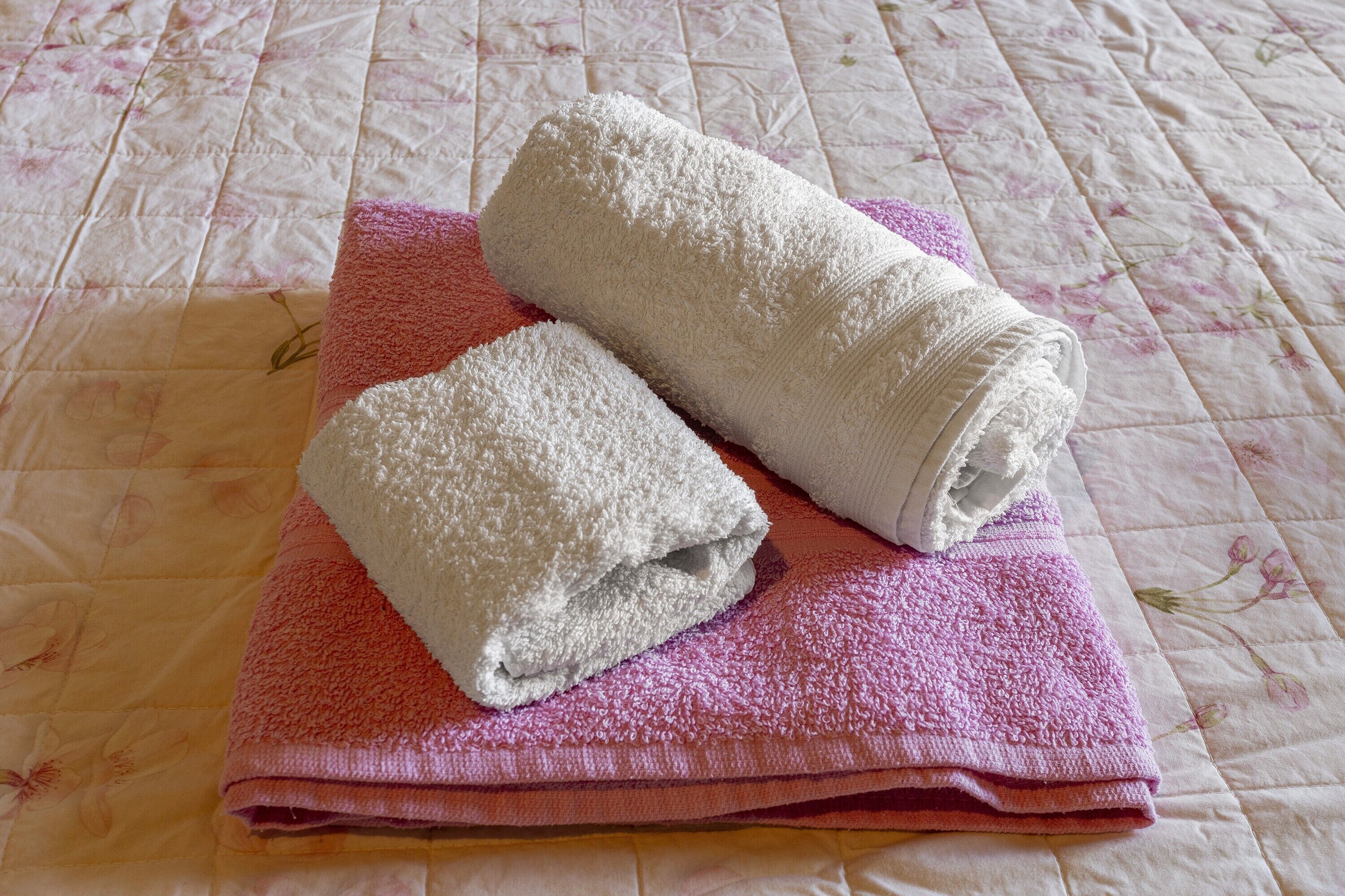 Two rolled towels on a pink towel on a bed with a floral patterned bedspread.