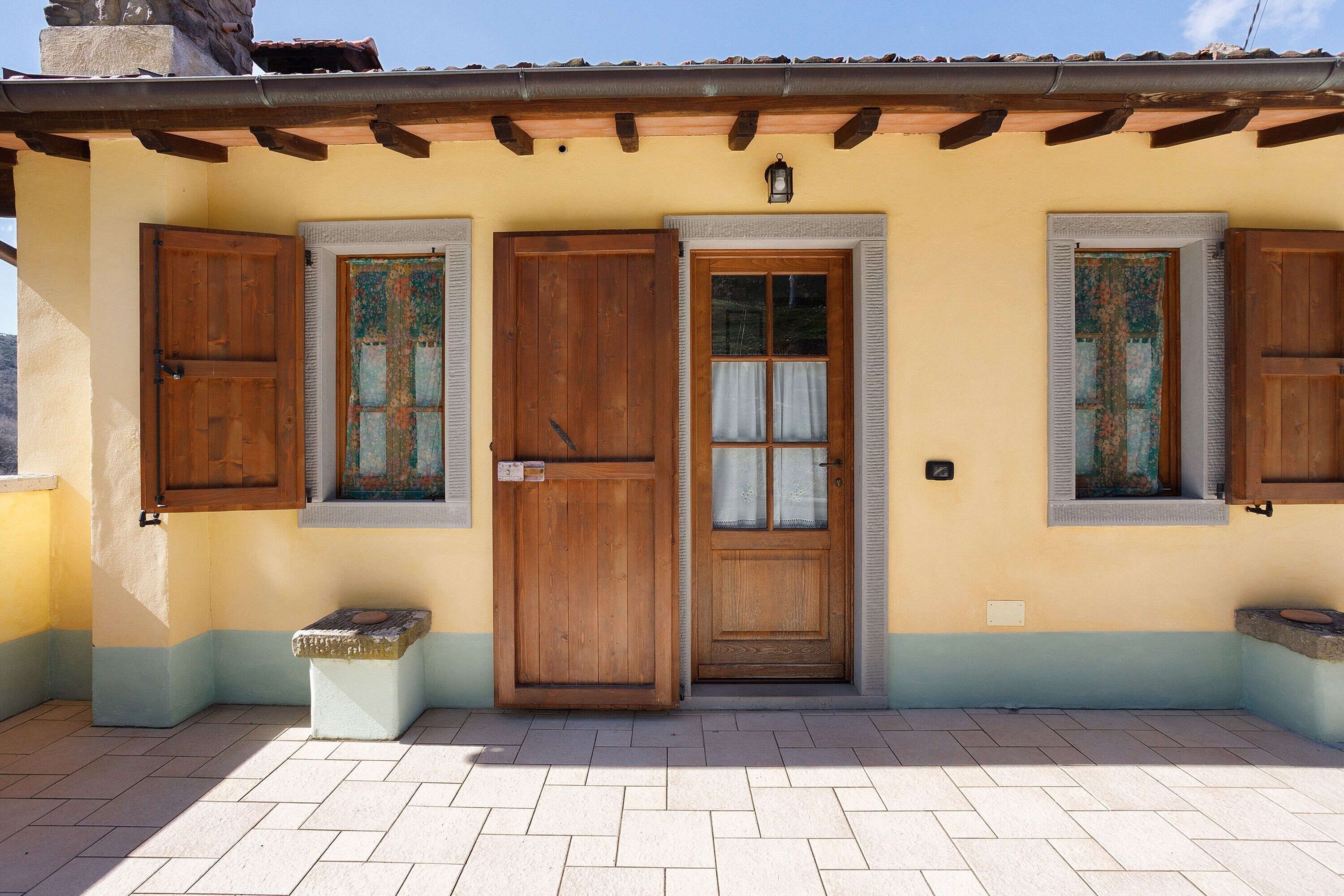 Un edificio con entrada de baldosas, puertas de madera y ventanas con contraventanas.