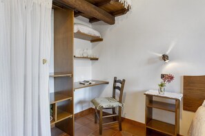 Une chambre à coucher avec un lit en bois, une chaise, une table de chevet ornée d’un vase, et une étagère sur laquelle se trouvent une carafe et des tasses.