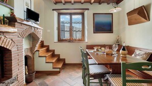 Un comedor con chimenea de ladrillo, escalera de madera y una mesa lista con sillas.