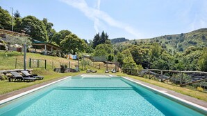 Una piscina con sillas de descanso, una zona de estar cubierta y vistas a colinas.