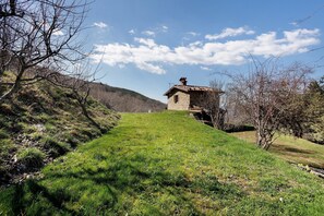A stone building with a sloped roof, surrounded by grassy terrain and trees.