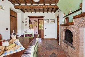 Ein Essbereich mit Holztisch, gedecktem Tisch für eine Mahlzeit, einem Kamin aus Ziegelsteinen und Blick in einen anderen Raum.