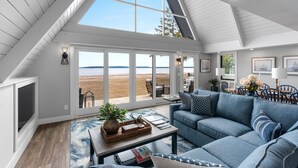 A spacious living room with a large window, a blue sofa, and a dining area with a view of the beach. - Moonlight Bay Retreat, Waterfront home near Cana Island. (Baileys Harbor)