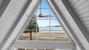 A room with a large window overlooking a beach, a ceiling fan, and a view of the ocean. - Moonlight Bay Retreat, Waterfront home near Cana Island. (Baileys Harbor)