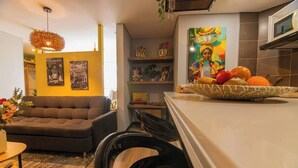 Un salon moderne avec un canapé, une table à manger agrémentée d’un vase de fleurs et un coin cuisine équipé d’un four à micro-ondes et d’un panier de fruits.
