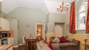 A cozy living room with a sofa and a dining table set for four. - Flagstaff Cottage (Saltash)