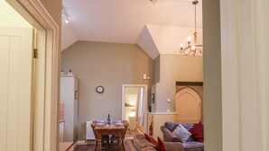 A dining area with a wooden table and chairs, a clock on the wall, and a sofa with red cushions. - Flagstaff Cottage (Saltash)