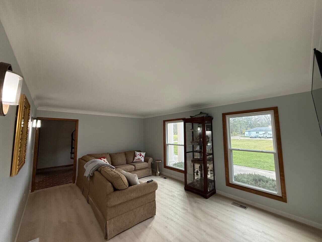 Un salon spacieux avec un canapé d’angle beige, un meuble vitré et de grandes fenêtres donnant sur l’extérieur.