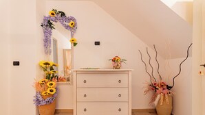 A room with a white dresser, a mirror, and two large flower arrangements. - Corte Manzoni B&B (Melendugno)