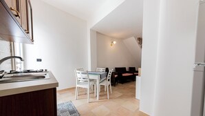 A kitchen with a sink, stove, and cabinets, a dining area with a table and chairs, and a living area with a sofa and chairs. - Corte Manzoni B&B (Melendugno)