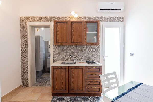 A compact kitchen with wooden cabinets, a built-in sink, and patterned backsplash tiles. - Corte Manzoni B&B (Melendugno)