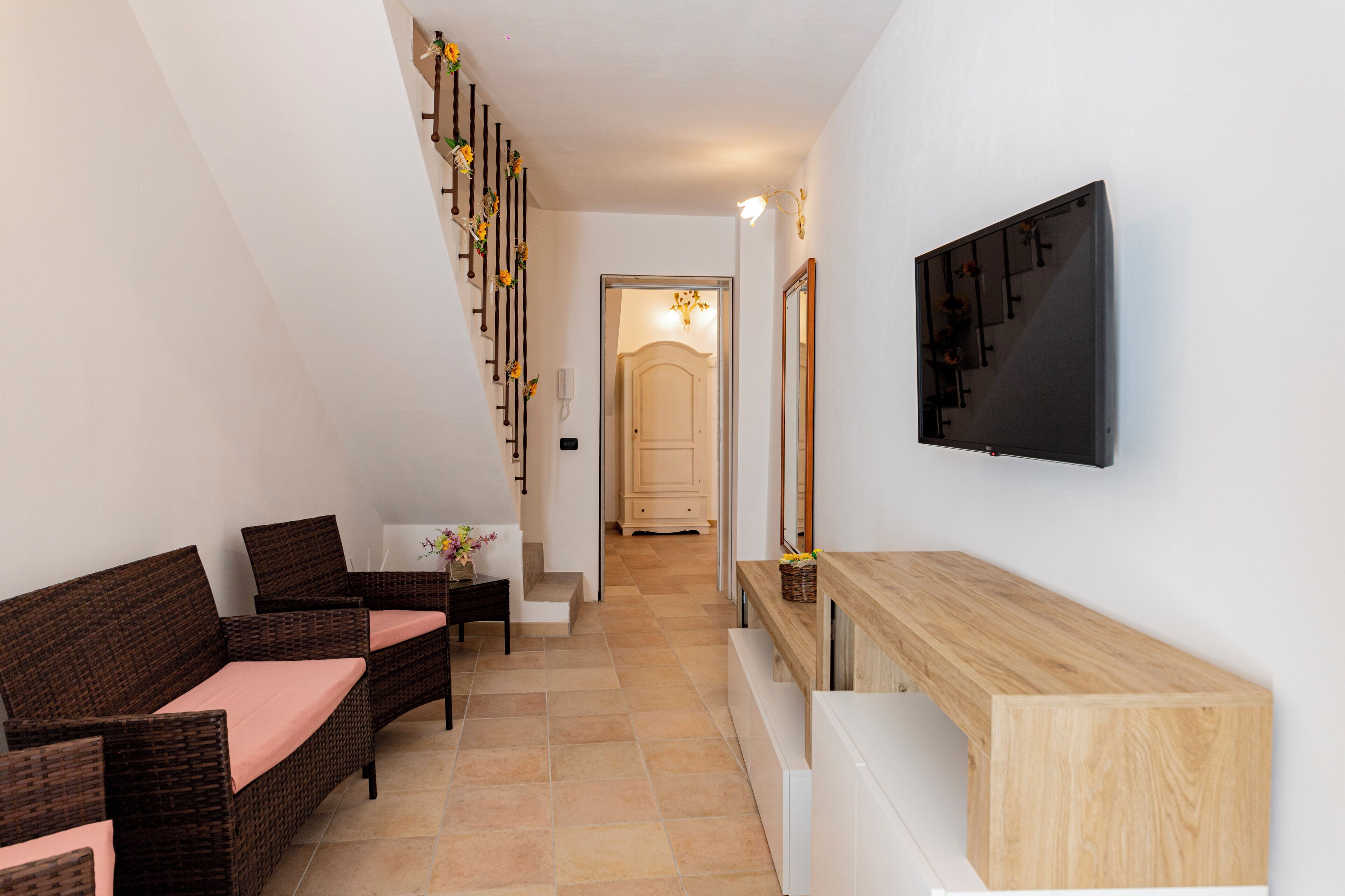 Un couloir aménagé avec des meubles en osier, une console en bois et un téléviseur fixé au mur.
