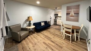 A compact living space with a sofa, a small table, a dining table with chairs, a kitchen area, and a painting on the wall. - Great Lakes Resort - Jr Suite - Suite 8 (Lexington)