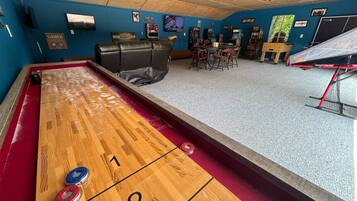 Et shuffleboard-bord med nummererede ender, et poolbord og et billardbord i et rum med blå vægge og diverse spillemaskiner.