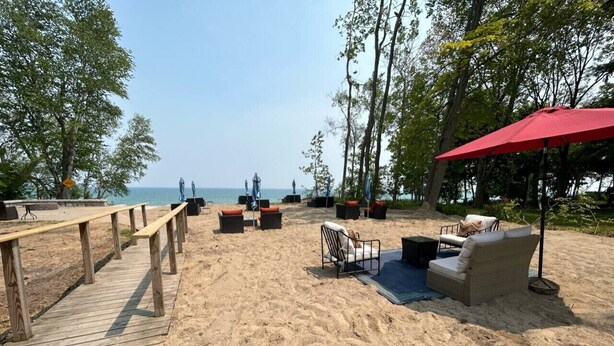 A beachside area with a wooden deck, outdoor seating, and a red umbrella. - Great Lakes Resort - Beach Studio - Suite 16 (Lexington)