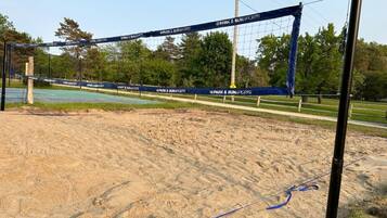 A volleyball net with "Park & Sun Sports" branding, set up on a sandy area with trees and a clear sky in the background.
