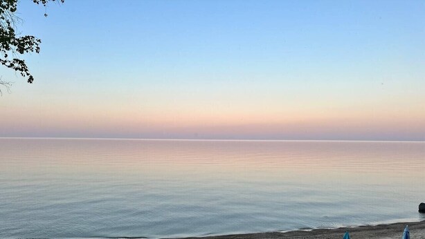 Une plage bordée d’une rangée de transats et de parasols, une mer calme et un ciel dégagé.