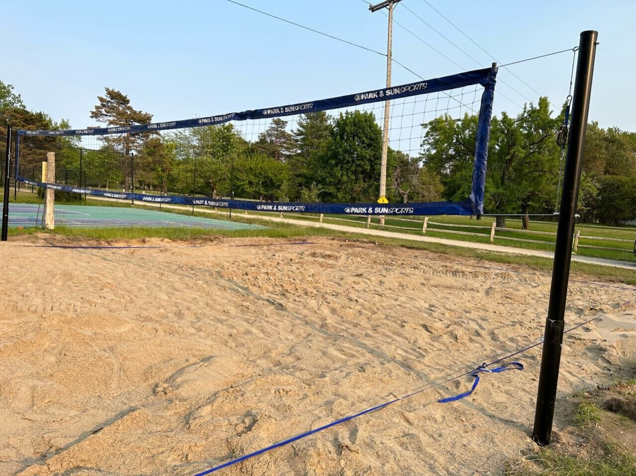 Een volleybalnet met de branding 'Park & Sun Sports', opgesteld op een zandbodem met een heldere lucht op de achtergrond.