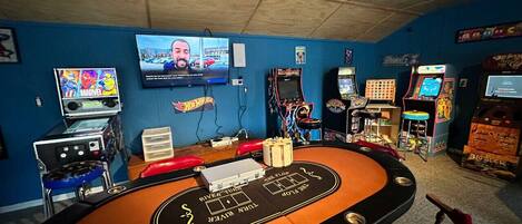 Salón de casino con mesa de billar, juegos de arcade y un televisor que muestra un noticiero.