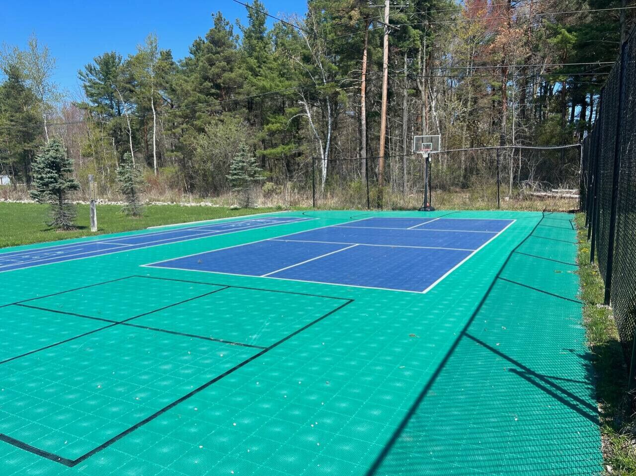 An outdoor tennis court with a net, surrounded by trees and a fence.