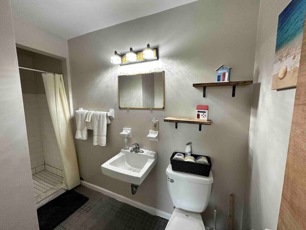 Ein Badezimmer mit Waschbecken, Spiegel und Toilette. Handtücher hängen an der Wand und eine Duschvorhang ist angebracht.