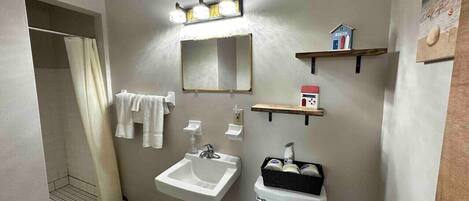 Ein Badezimmer mit Waschbecken, Spiegel und Toilette. Handtücher hängen an der Wand und eine Duschvorhang ist angebracht.