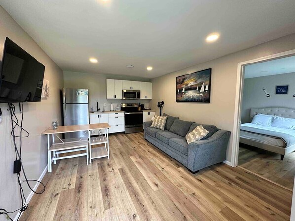 A compact living space with a kitchenette, a gray sofa, a dining table, and a bed.
