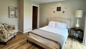 A bedroom with a bed, a chair, a bedside table with a lamp, and a sign on the wall. - Great Lakes Resort - Family Suite - Suite 2 (Lexington)