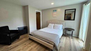 A bedroom with a bed, a chair, a bedside table, and a mirror. - Great Lakes Resort - Family Suite - Suite 3 (Lexington)