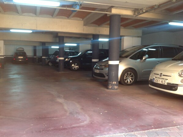 En parkeringskælder med flere biler parkeret i rækker, betonstolper og et fladt loft.