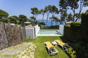 Ein Garten mit Swimmingpool, zwei Liegestühlen und einem gepflasterten Weg zum Pool.