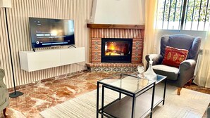 A modern living room with a flat-screen TV, a fireplace, a comfortable armchair, and a glass coffee table. - Casa Rural Lomalinda: Mountain Views, Wi-Fi, and Air Conditioning (Granada)