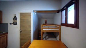 Una habitación pequeña con una cama individual encima de otra, una mesa de madera, una ventana y una puerta.