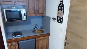 Una cocina compacta con armarios de madera, un microondas, un fregadero y un refrigerador pequeño.