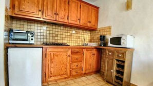 A compact kitchen with wooden cabinets, a white refrigerator, a microwave, and a gas stove. - Appa L'olivier 18 rue Louis Pasteur (Saintes-Maries-de-la-Mer)