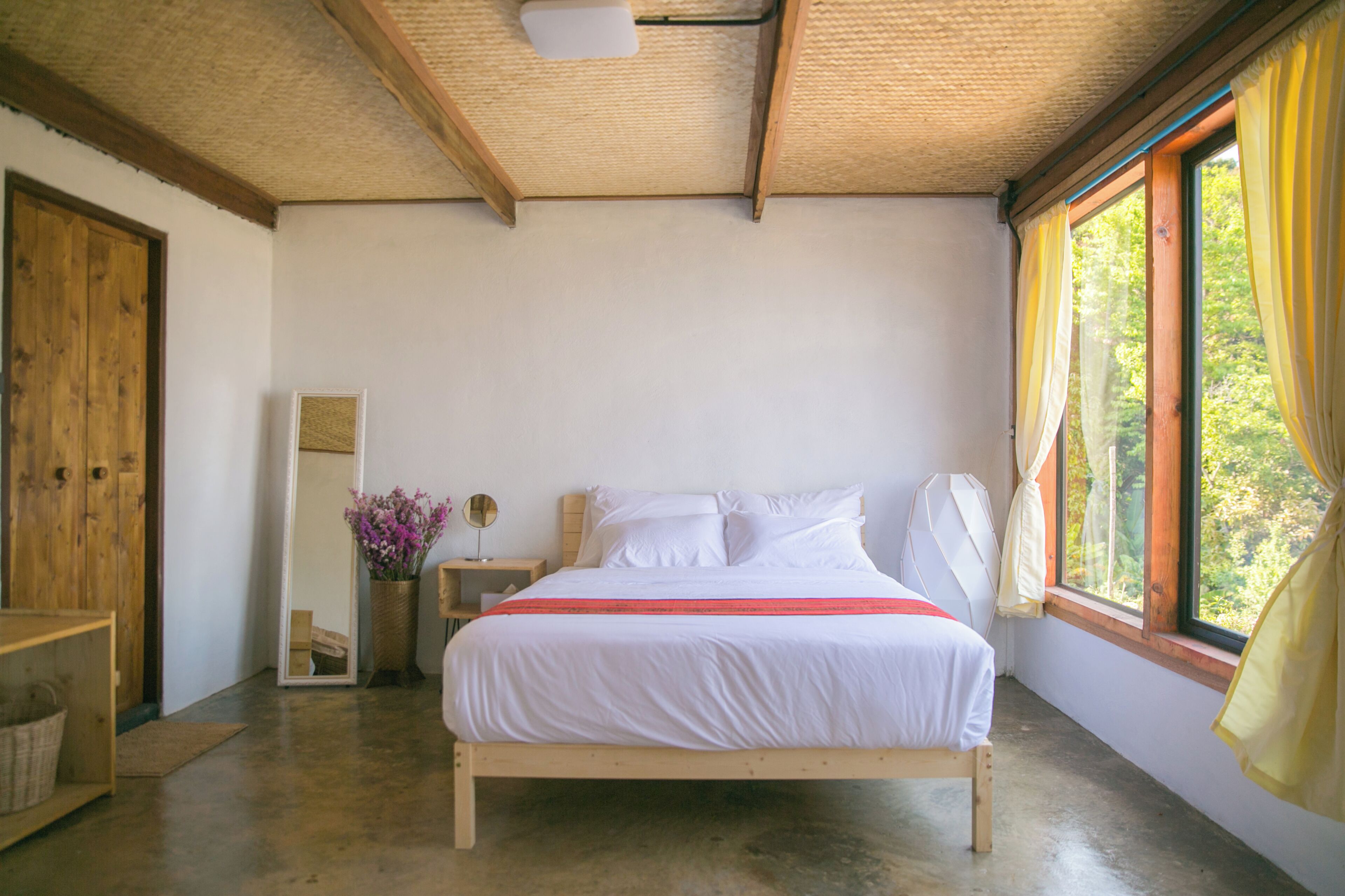 A bedroom with a wooden bed, a mirror, a bedside table, and a window with curtains.