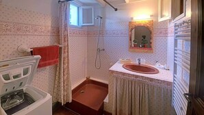 Et lille badeværelse med bruser, håndvask og et vindue.