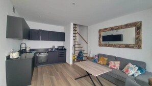 Eine moderne Küche mit dunklen Schränken, einem Esstisch und einem grauen Sofa mit bunten Kissen.