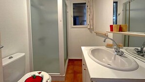 Et badeværelse med bruser, toilet, håndvask og et lille vindue.