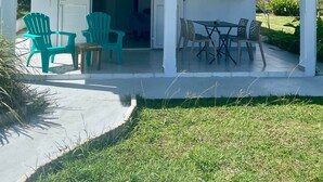 Un espace extérieur abrité, avec une table et des chaises, une porte portant l’inscription « Paradis » et un petit jardin.