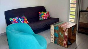 Un salon avec un canapé foncé, des coussins colorés, un fauteuil turquoise et une table basse rustique.
