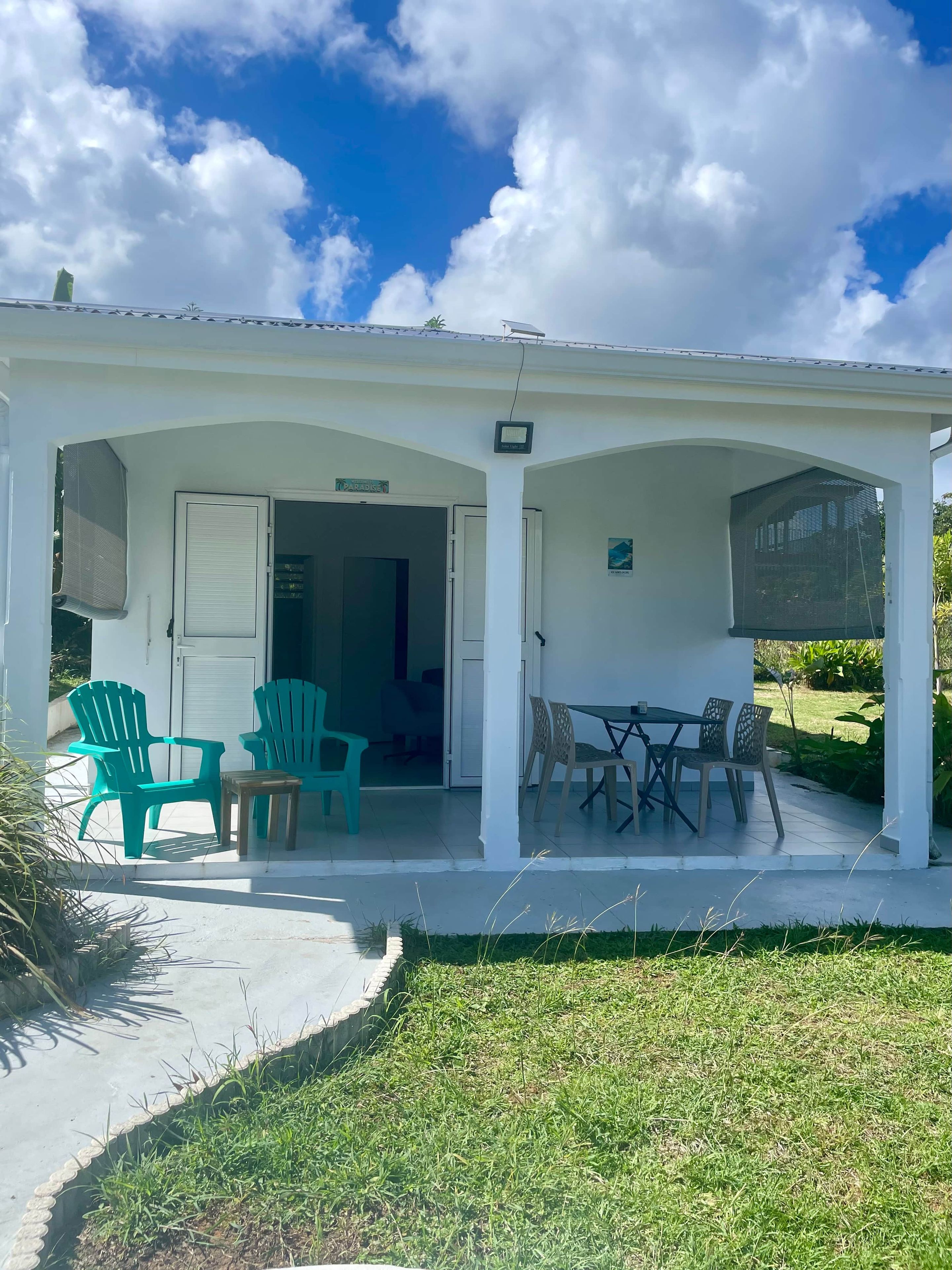 Un espace extérieur abrité, avec une table et des chaises, une porte portant l’inscription « Paradis » et un petit jardin.